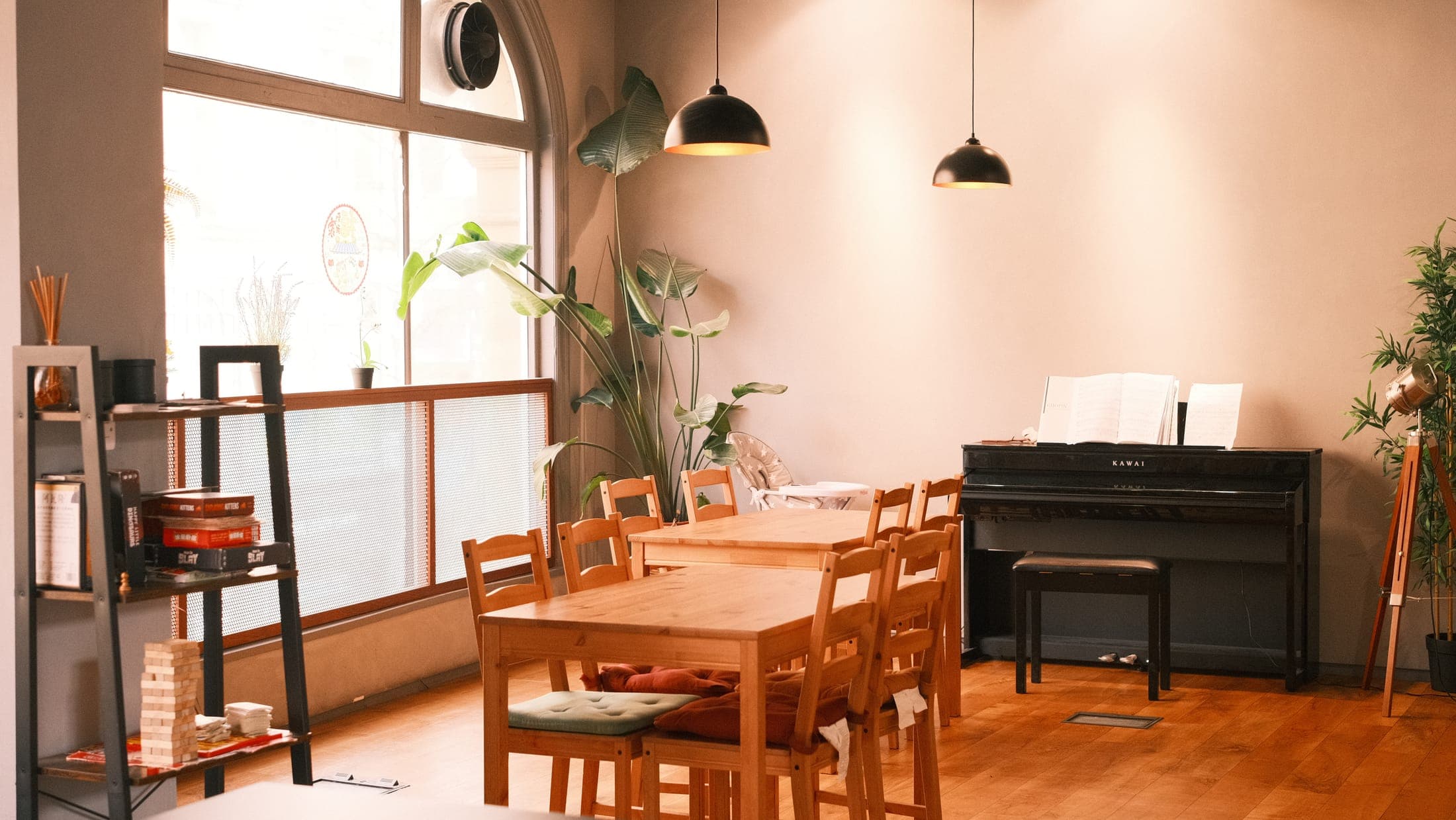The warm room inside Mr Tea — wooden tables and chairs, a piano, and leafy plants by a tall arched window
